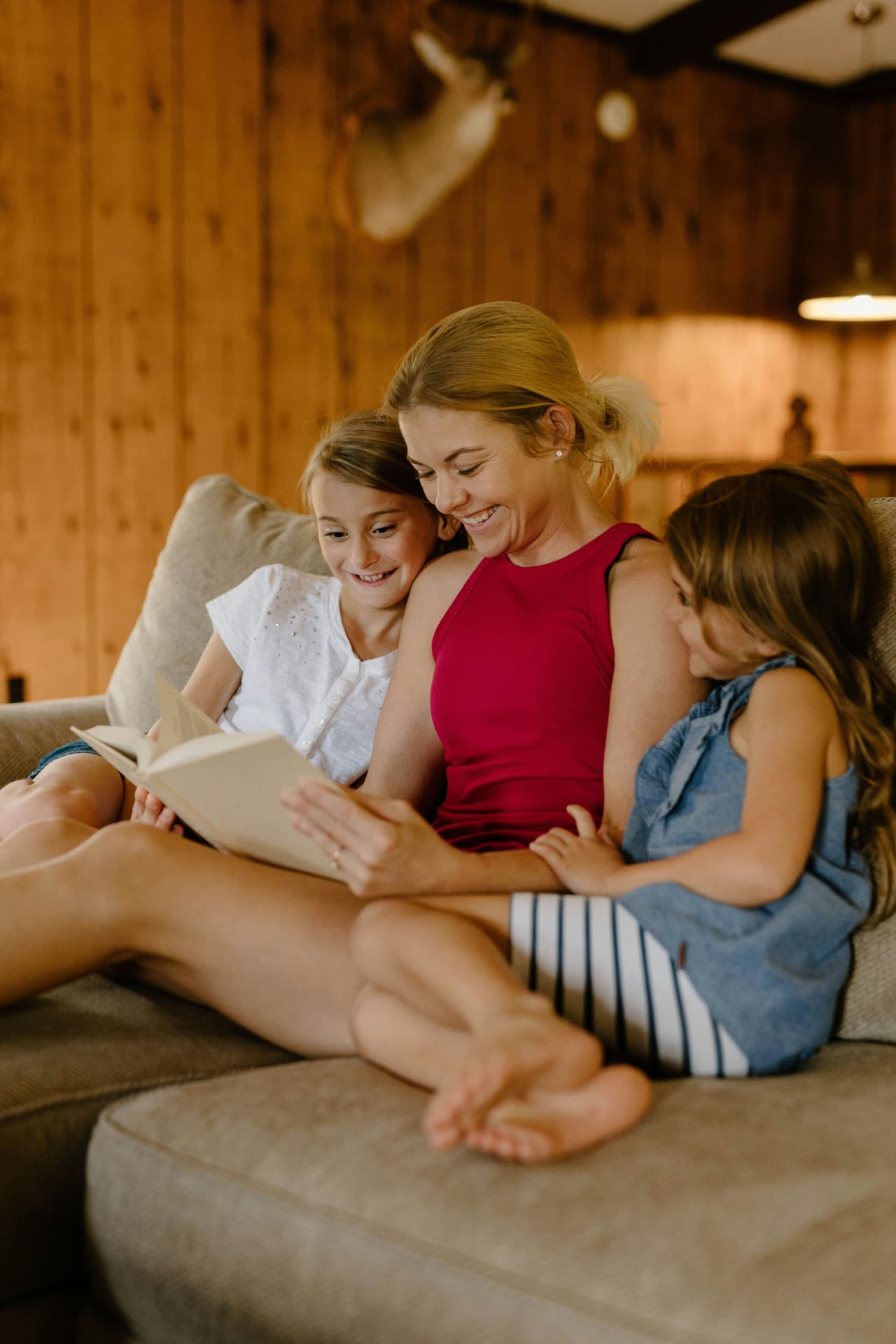 A young woman reading an open book with two girls on a sofa